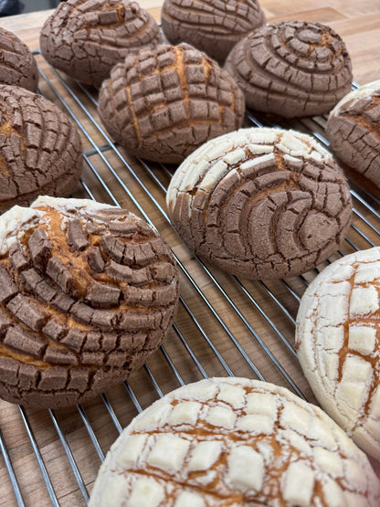 Freshly baked Mexican conchas with a soft, fluffy interior and a crispy sugar topping in vanilla and chocolate flavors, displayed at Shelíss Bakeshop in Toronto